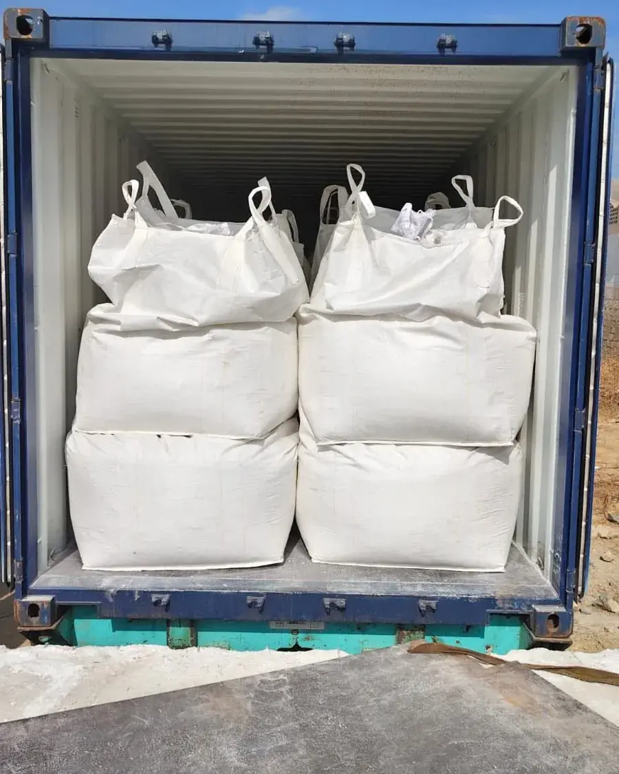 White jumbo bags stacked inside a blue shipping container.